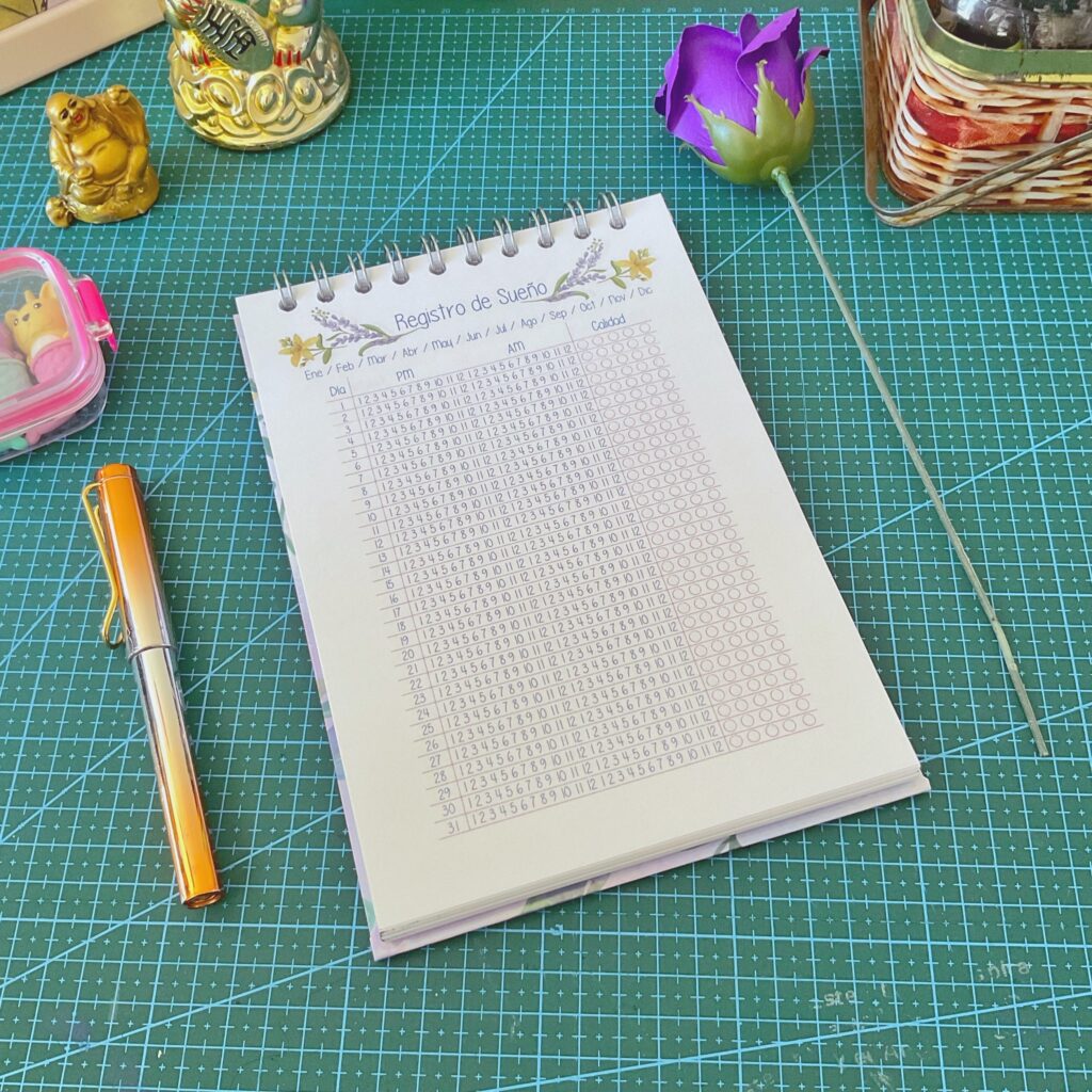 Página interior del cuaderno de terapias, es la seccion de registro del sueño diario. Está sobre una base de corte verde con objetos como un lápiz naranja y figuras decorativas alrededor.