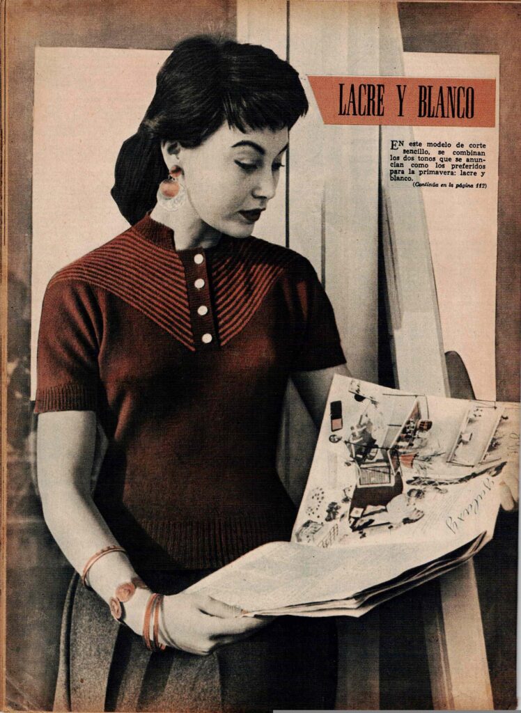 Mujer joven con peinado vintage y labios pintados de rojo, vestida con un suéter de punto en color lacre con detalles blancos y rayas diagonales en el pecho. Está de pie junto a una pared clara, sosteniendo una revista abierta con imágenes de interiores. El texto en la imagen dice 'Lacre y Blanco' y menciona una combinación de colores de moda para la primavera. 
