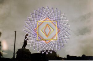 Fotografía analoga de monumento a Arturo Prat en la ciudad de Punta Arenas, intervenida con figura geometrica simetrica estilo mandala e, colores lilas y naranjos.