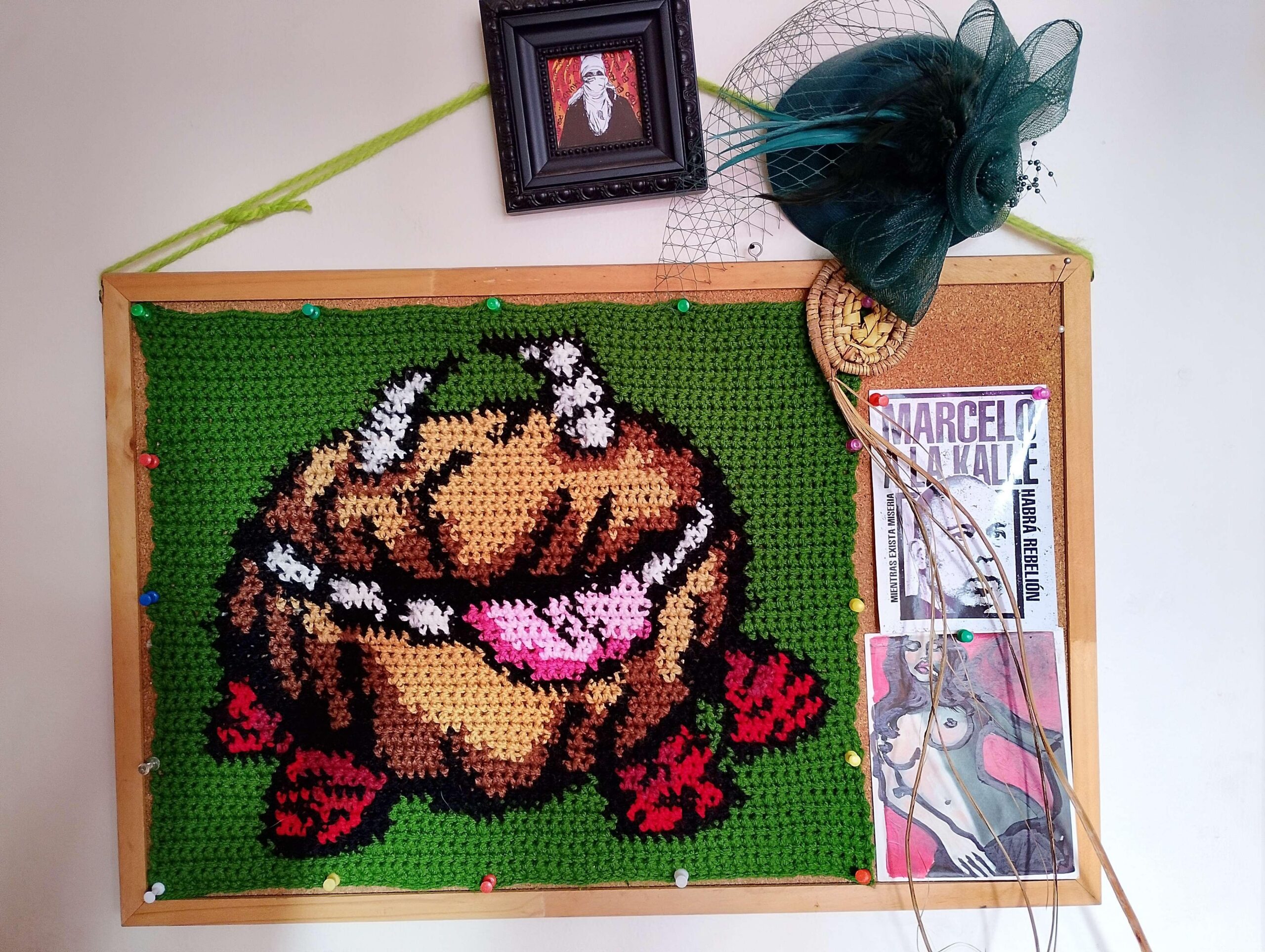 Fotografiá de pizarra de corcho colgada en una pared blanca, sobre la pizarra se encuentra colgado un tejido a crochet/ganchillo del personaje Chester